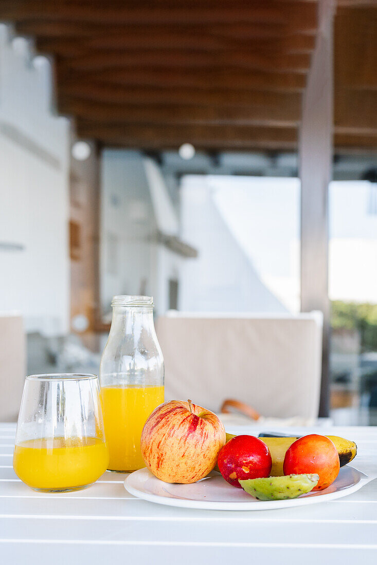 Köstliche halbierte Papaya auf einem Teller neben verschiedenen bunten Früchten und einem Glas frischen Orangensaft auf einem weißen Tisch auf der Terrasse an einem sonnigen Sommertag