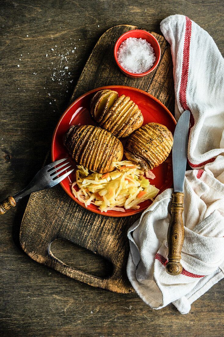 Baked Hasselback potatoes with spices and fermented cabbage salad served in bowl on wooden table