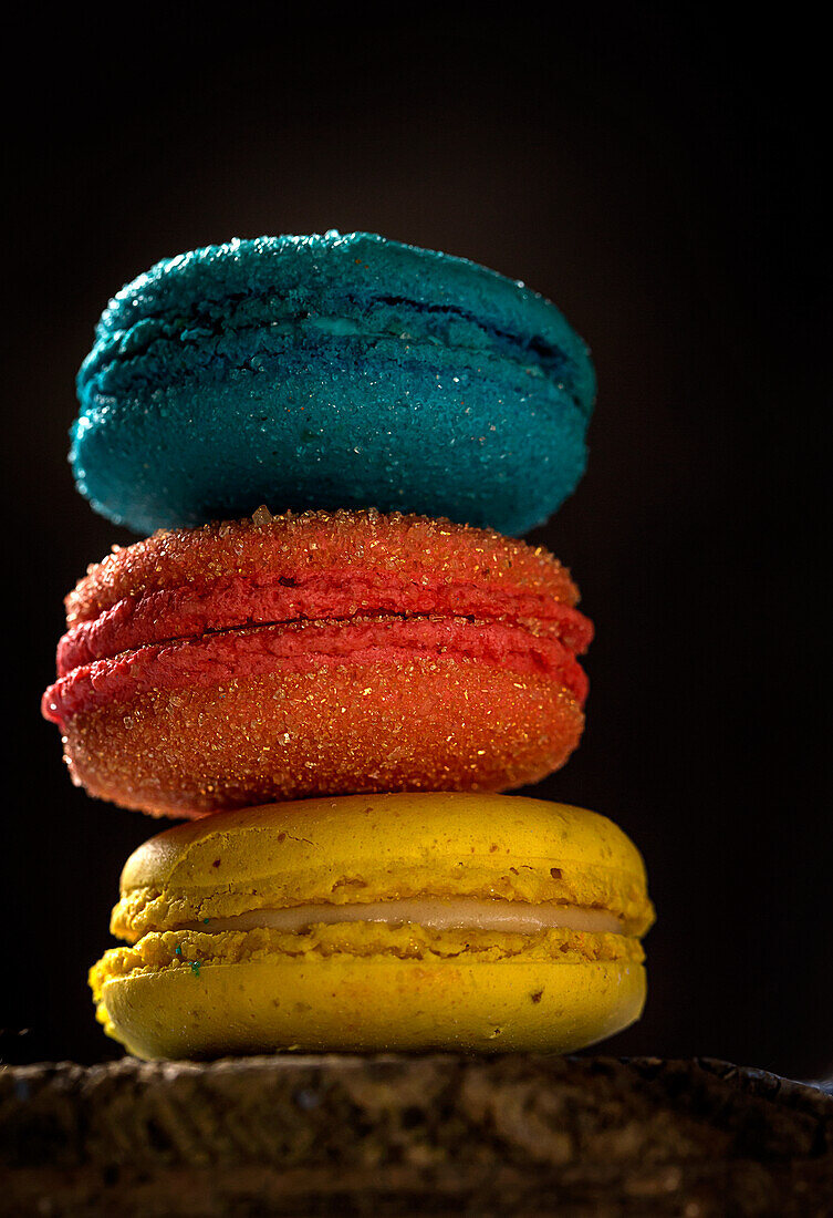 Close up of colorful French macaroons with various fillings placed on wooden table in dark background