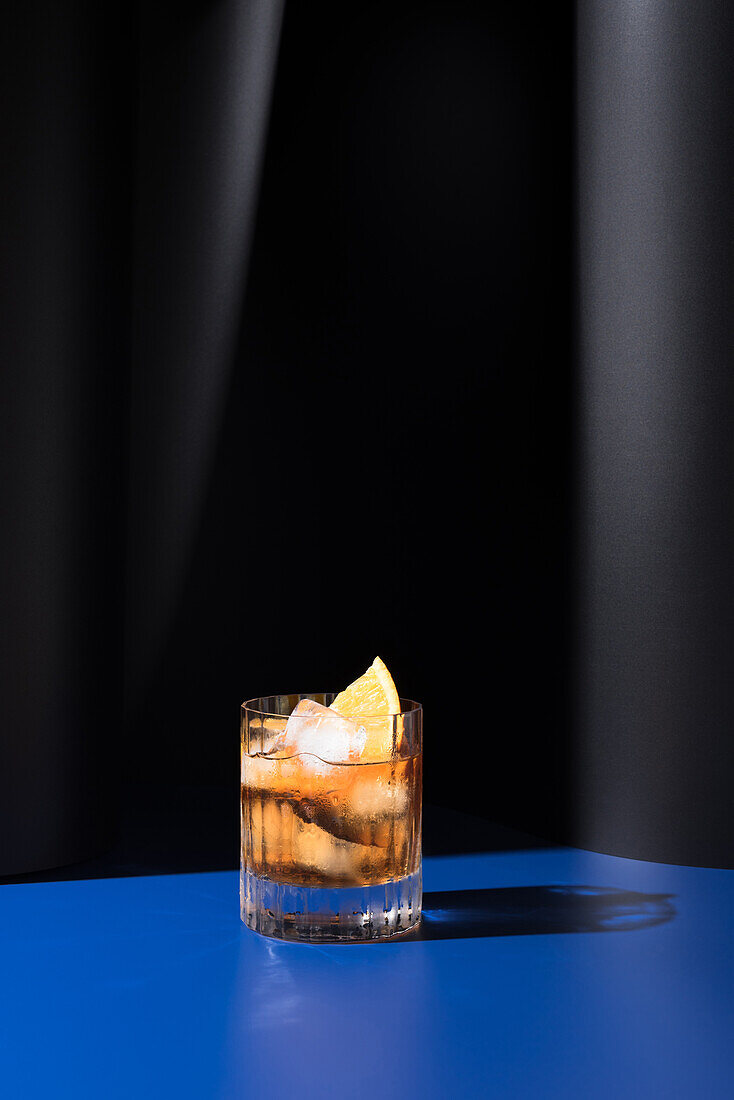 Glas alkoholischer Cocktail mit rotem Wermut, serviert mit Orangenscheiben in einem hellen Studio mit blauer und schwarzer Wand