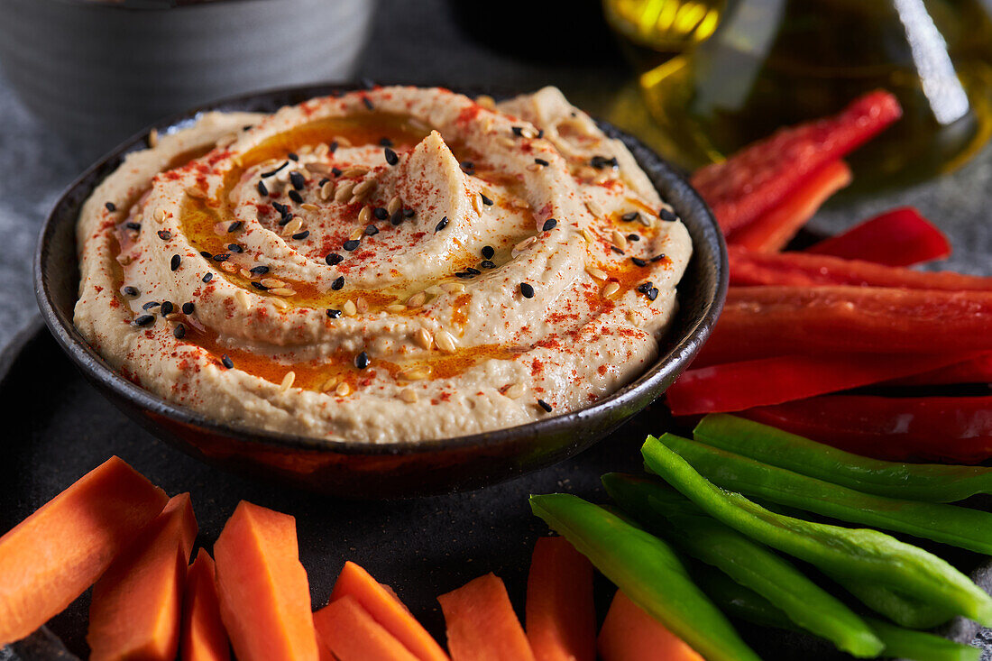 Blick von oben auf köstlichen Hummus und verschiedene Gemüsescheiben, die neben einer Flasche mit Öl auf einem grauen Marmortisch serviert werden