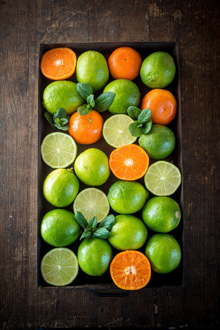 Von oben reife grüne Limetten und Orangen in einer Kiste auf einem rustikalen Holztisch