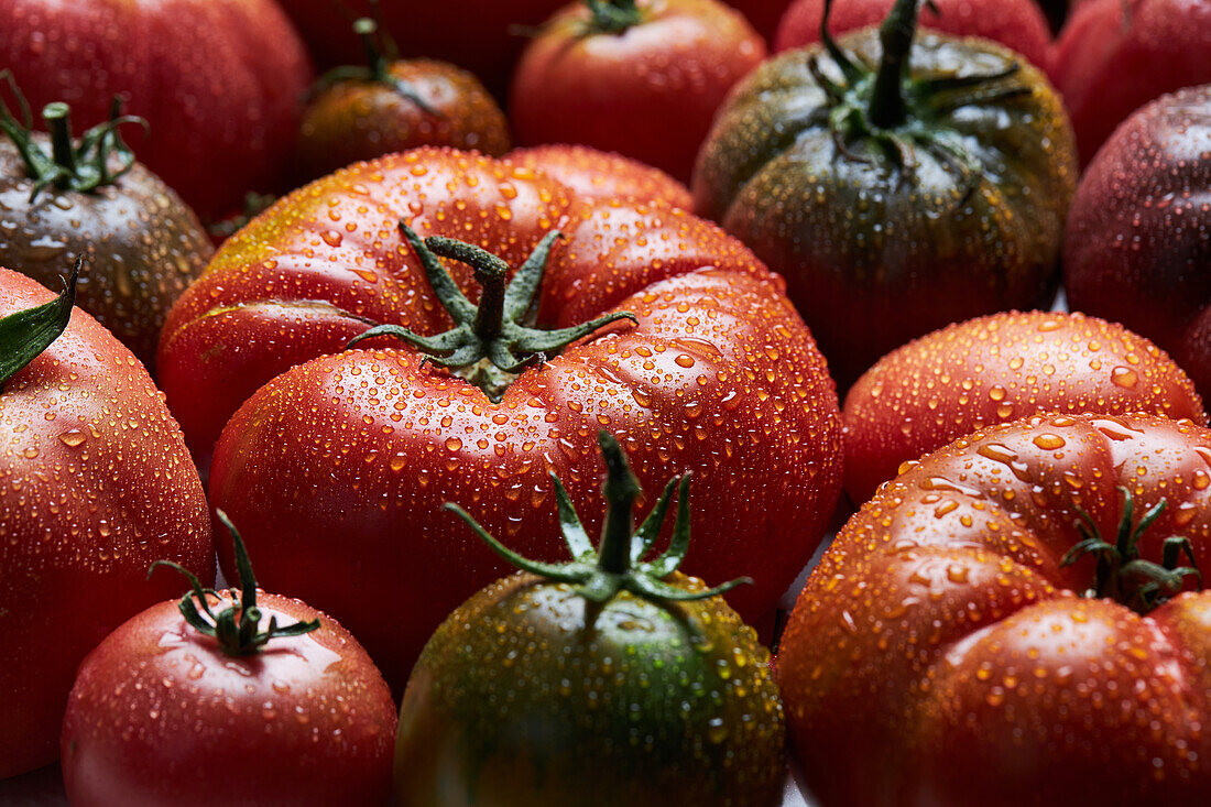 From above of appetizing fresh ripe tomatoes with drops of water with green leaves