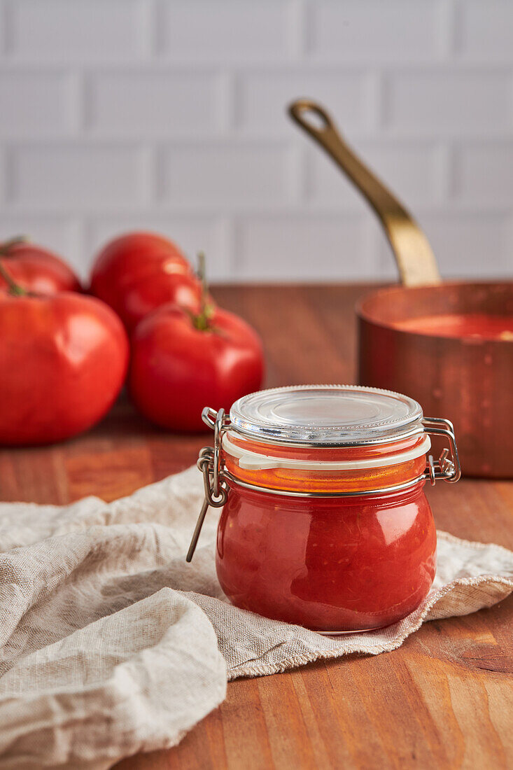 Glasgefäß mit frischer Tomatensauce auf gewebter Matte in der Küche zu Hause