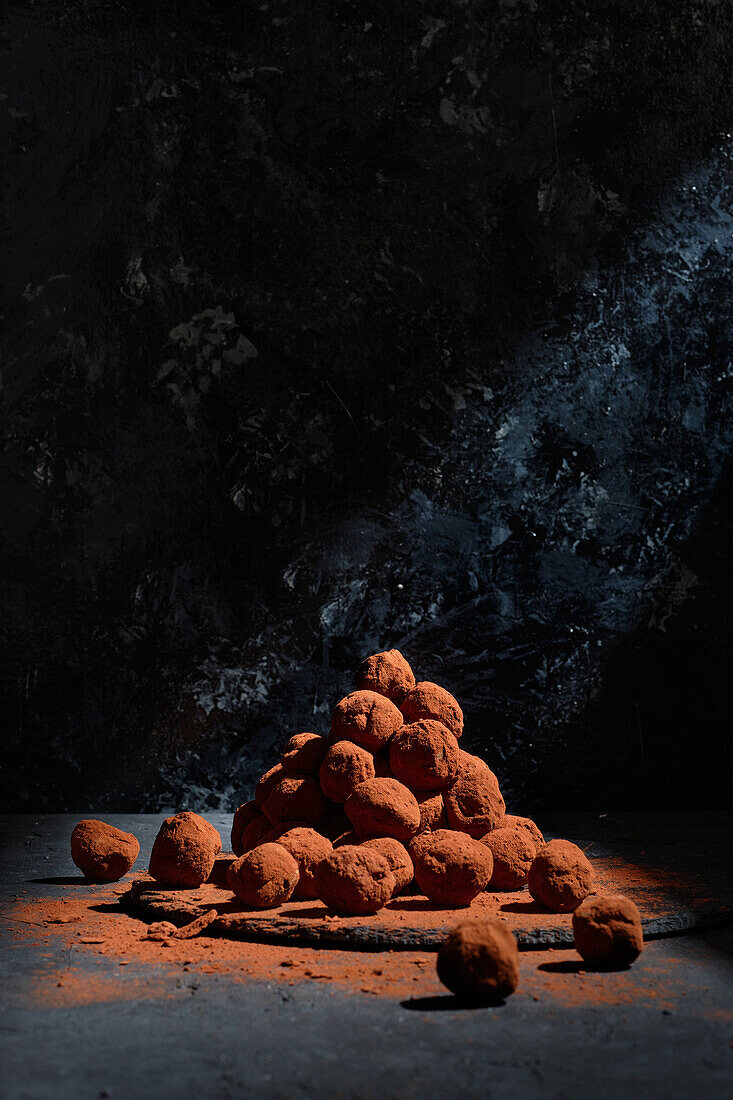 Haufen köstlicher Schokoladentrüffel in Form von Kugeln auf einem Tisch vor dunklem Hintergrund in einem Studio