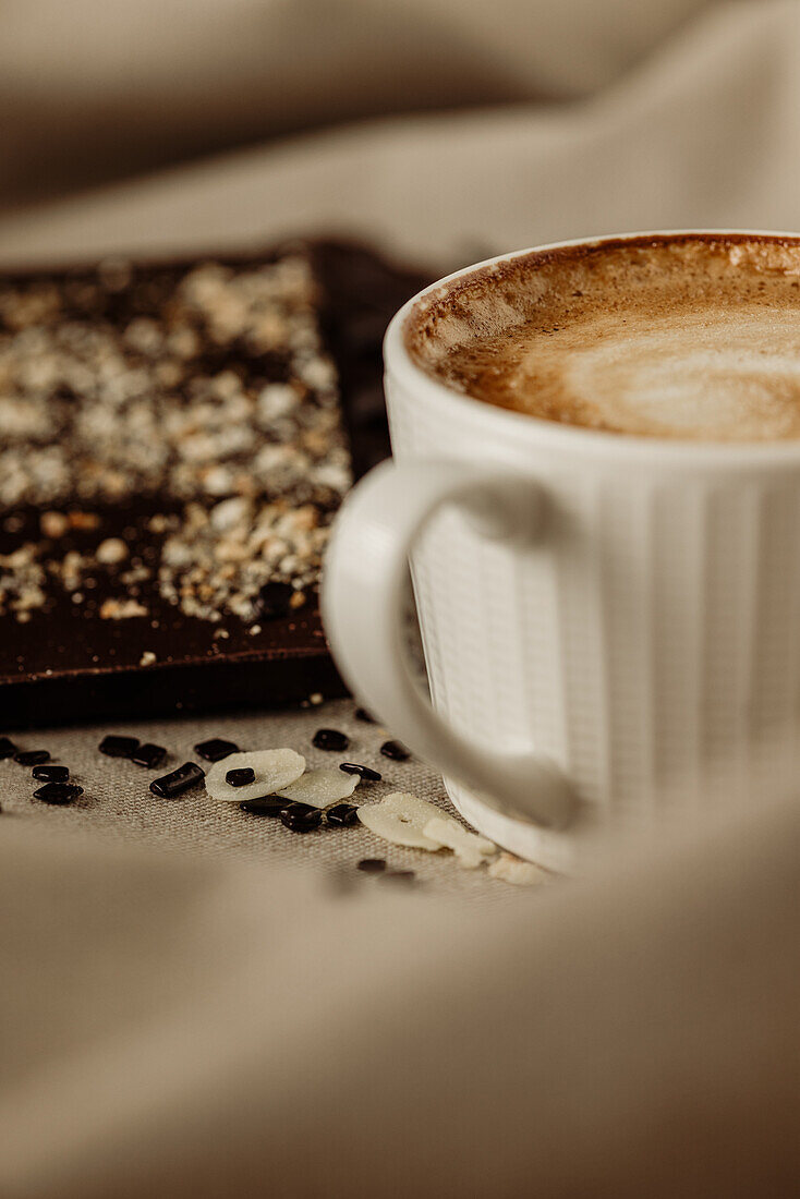 From above of cup of hot aromatic coffee with foam placed on wooden table and chocolate bar