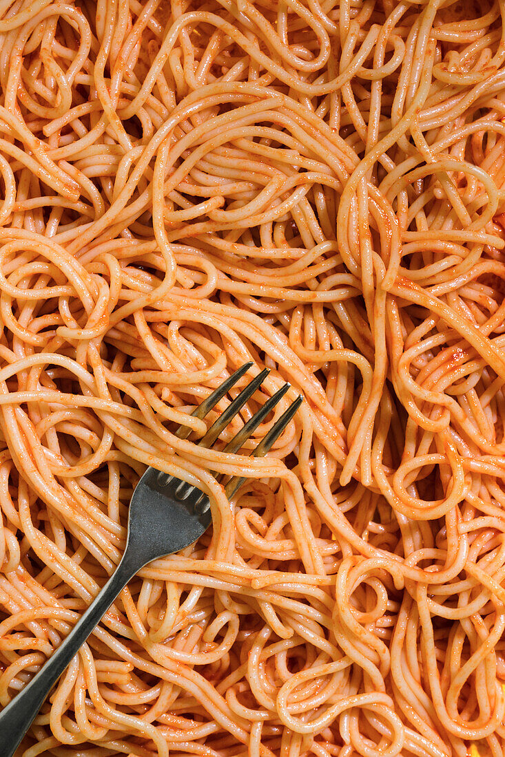 Von oben appetitliche Spaghetti mit roter Soße und Gabel auf gelbem Hintergrund