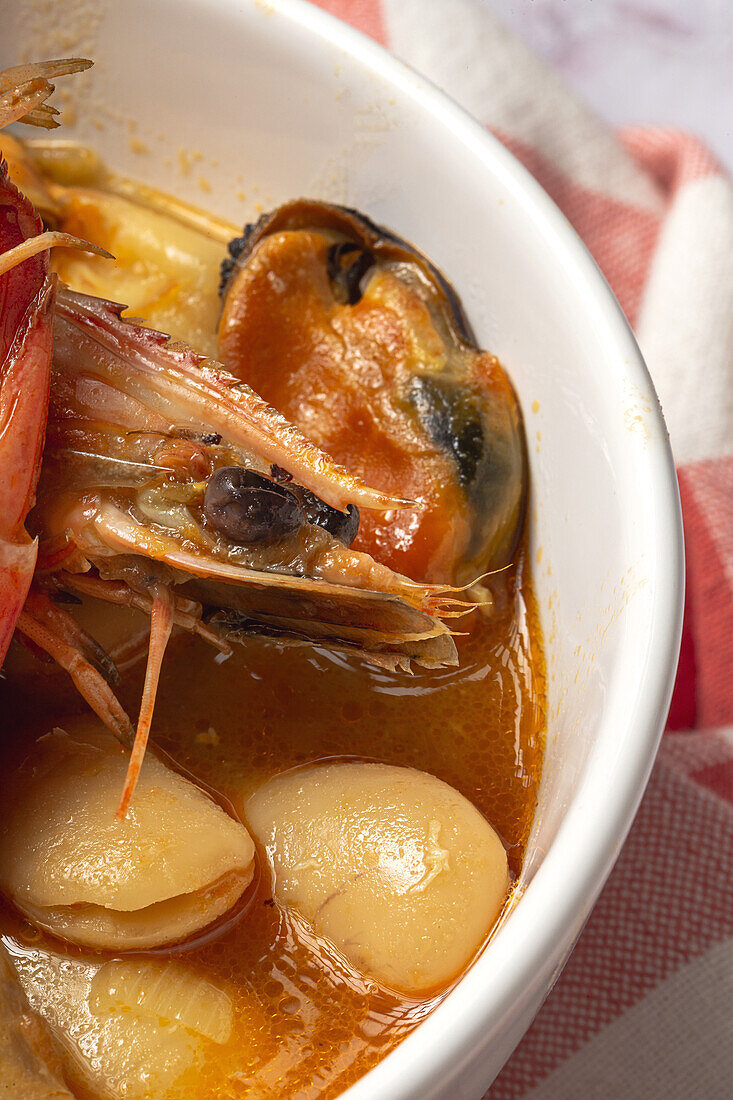 Nahaufnahme einer Schüssel mit einem typischen Bohneneintopf mit Garnelen, Krabben und Muscheln auf einem rot karierten Steintisch