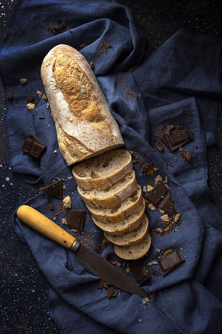 Hoher Winkel eines frisch gebackenen Brotlaibs mit Schokoriegeln und Messer auf einer blauen Serviette auf dem Küchentisch