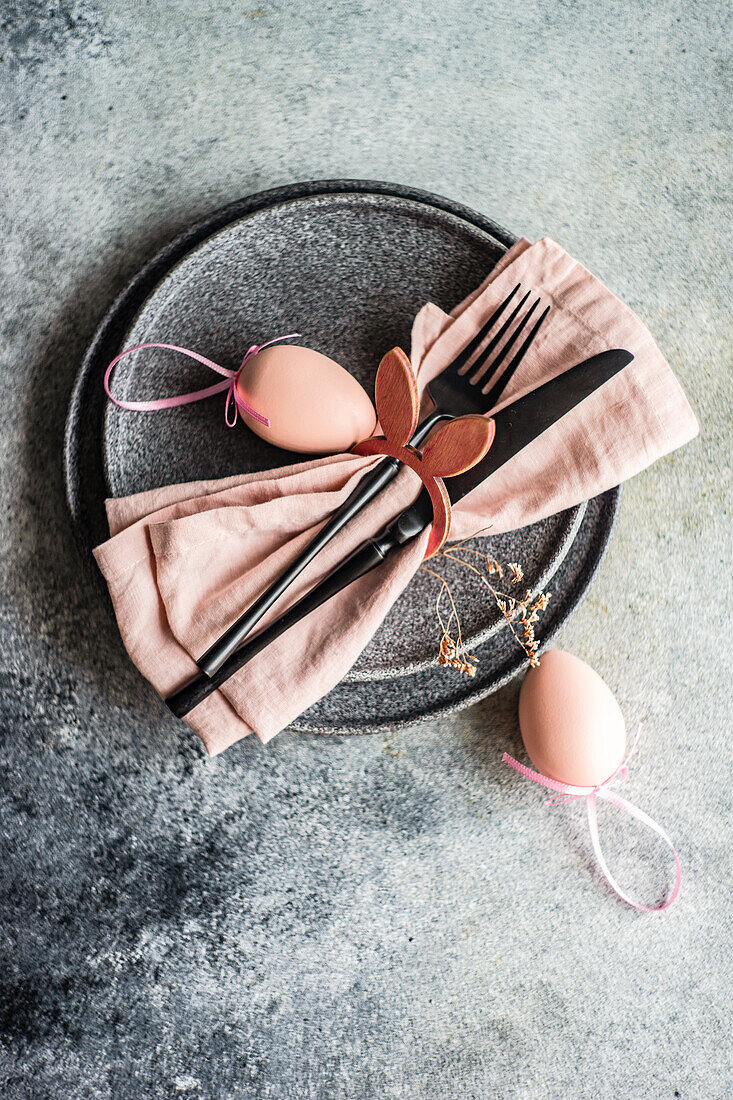 From above table set for Easter dinner with pink napkin and eggs on concrete background