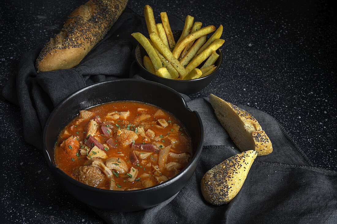 From above of tasty callos a la madrilena in black bowl near French fries and bread with seeds