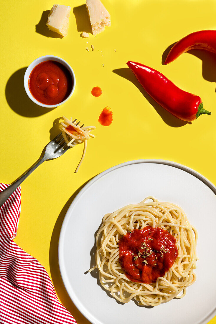 Von oben appetitanregende frisch gekochte Spaghetti mit roter Soße und Gewürzdip, rote Paprika, Käse und Gabel auf gelbem Hintergrund