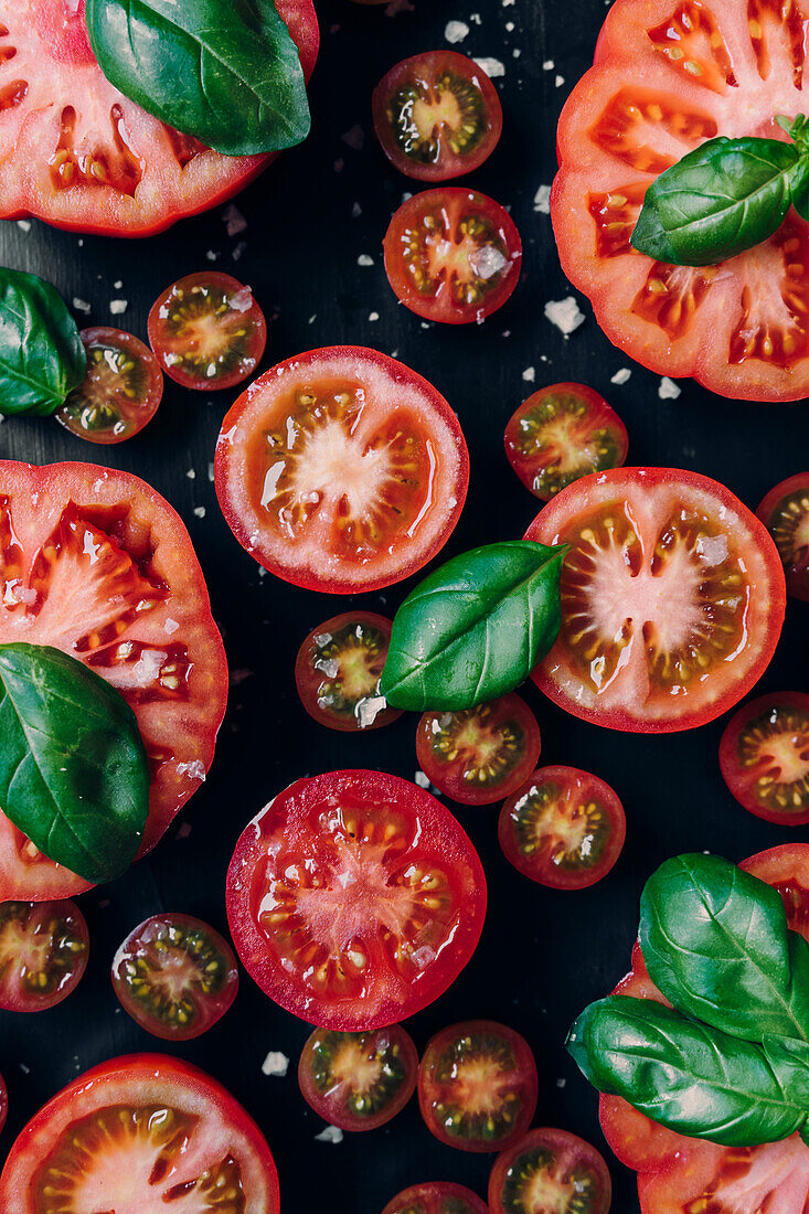 Von oben halbierte Tomaten auf einem Tisch mit Basilikumblättern