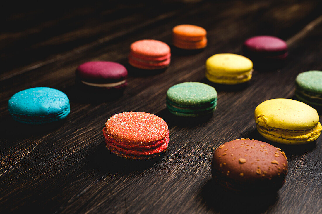 Colorful French macaroons with various fillings placed on wooden table in dark background
