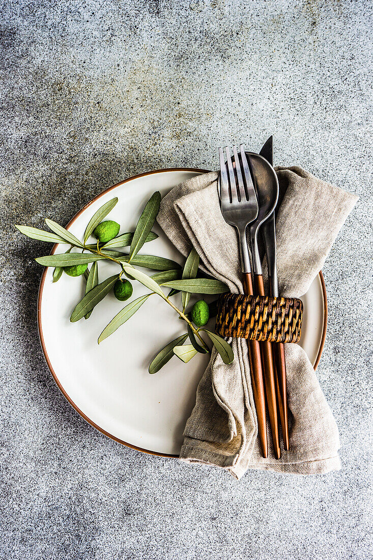 Rustikal gedeckter Sommertisch mit Tellern und Besteck, dekoriert mit Olivenzweigen