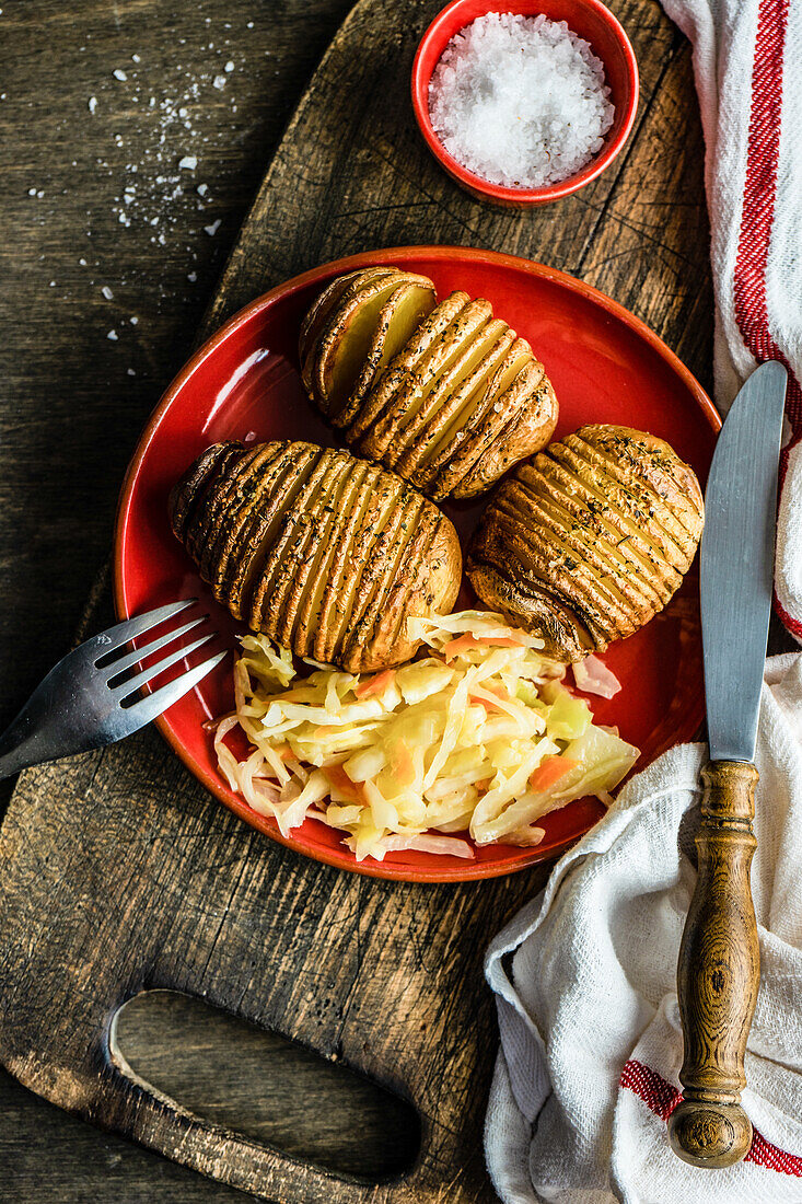 Gebackene Hasselback-Kartoffeln mit Gewürzen und fermentiertem Krautsalat, serviert in einer Schüssel auf einem Holztisch