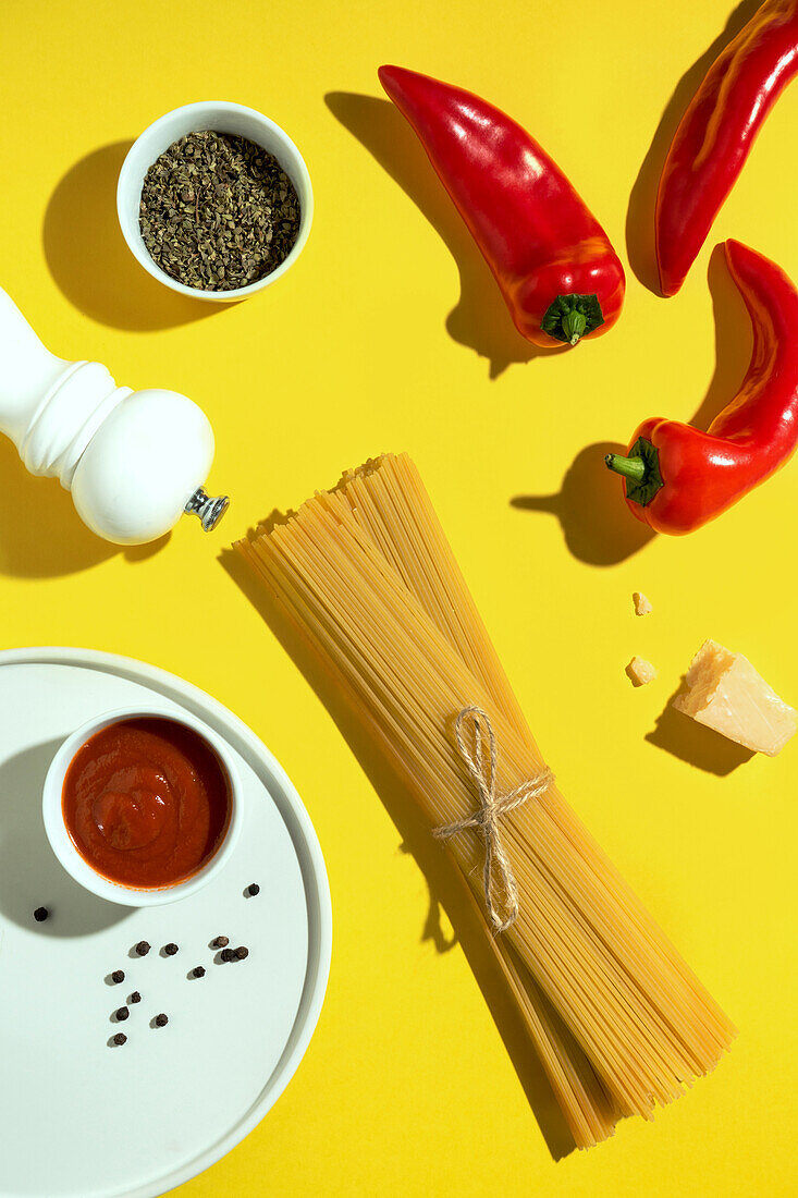 From above appetizing fresh dry spaghetti with red sauce and spice dip red peppers on yellow background