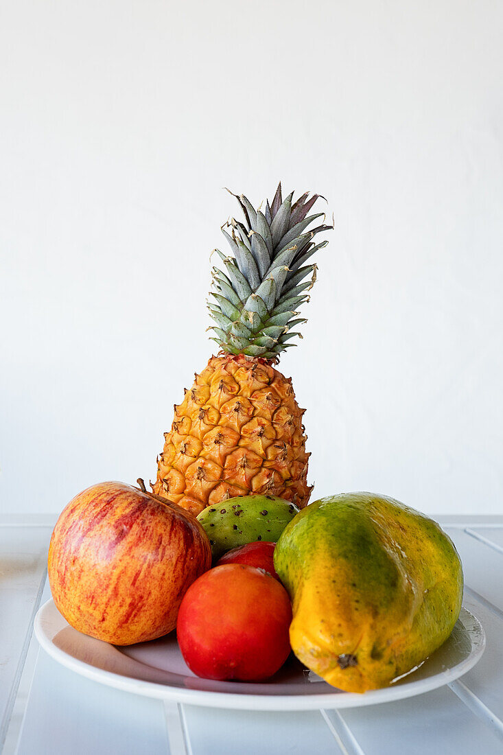 Delicious halved papaya served on plate near assorted colorful fruits and glass of fresh orange juice placed in white table