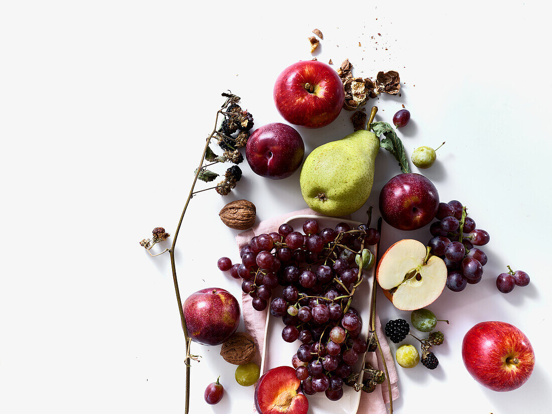 Composition with fresh summer fruits and berries on white background. Grapes, plums and apples in sunlight.