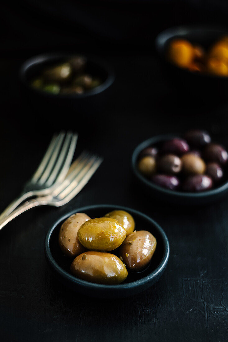 From above tasty juicy green brown yellow olives in black and white bowls on black table decorated with