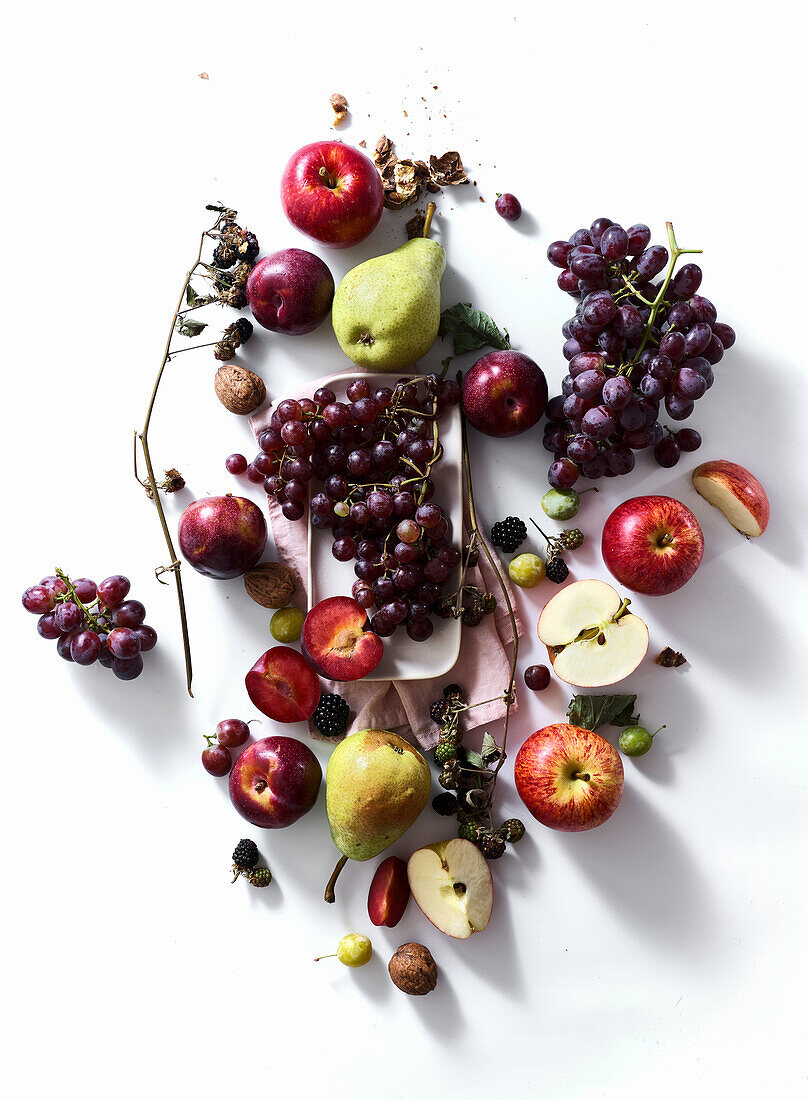 Composition with fresh summer fruits and berries on white background. Grapes, plums and apples in sunlight.