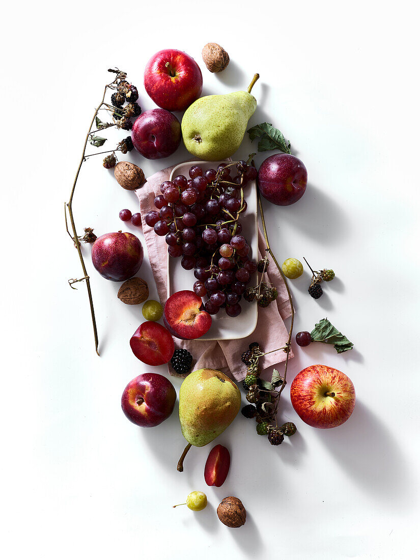 Composition with fresh summer fruits and berries on white background. Grapes, plums and apples in sunlight.