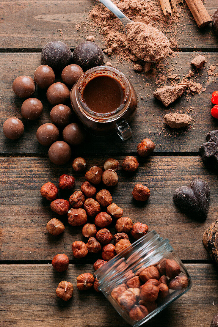 Draufsicht auf verschiedene handgemachte Pralinen mit Nüssen auf Holztisch mit Erdnussbutter und Zimtstangen