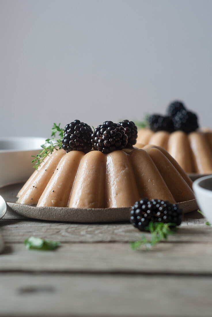 Nahaufnahme einer servierten veganen Panna Cotta mit Pfirsich und glänzenden süßen Brombeeren