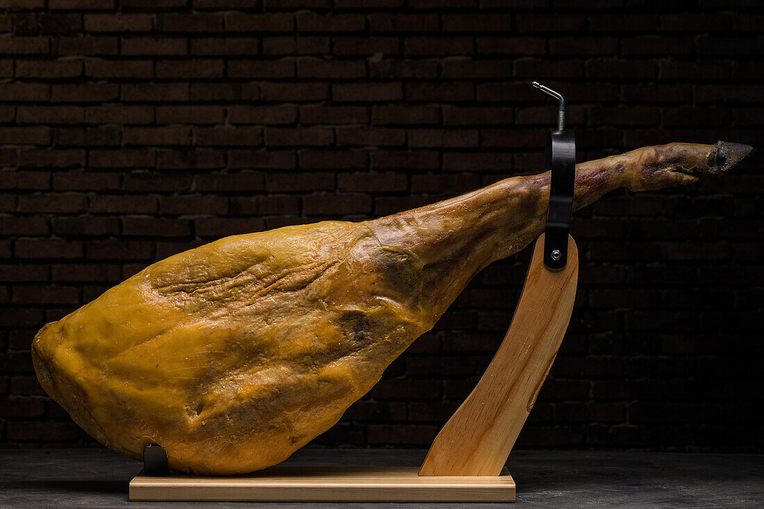 Delicious dry cured Spanish pork leg on wooden holder on gray surface