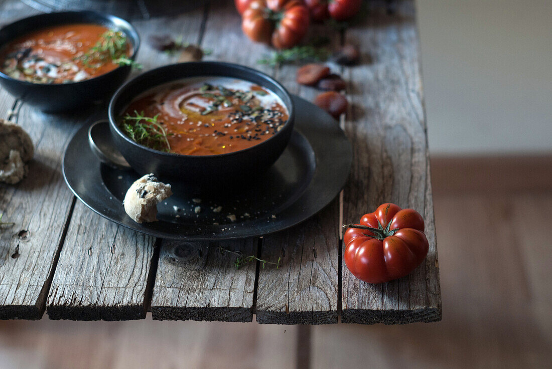 Flat lay of bowls with creamy tomato soup garnished with seeds and served on table with tomatoes and dried apricots