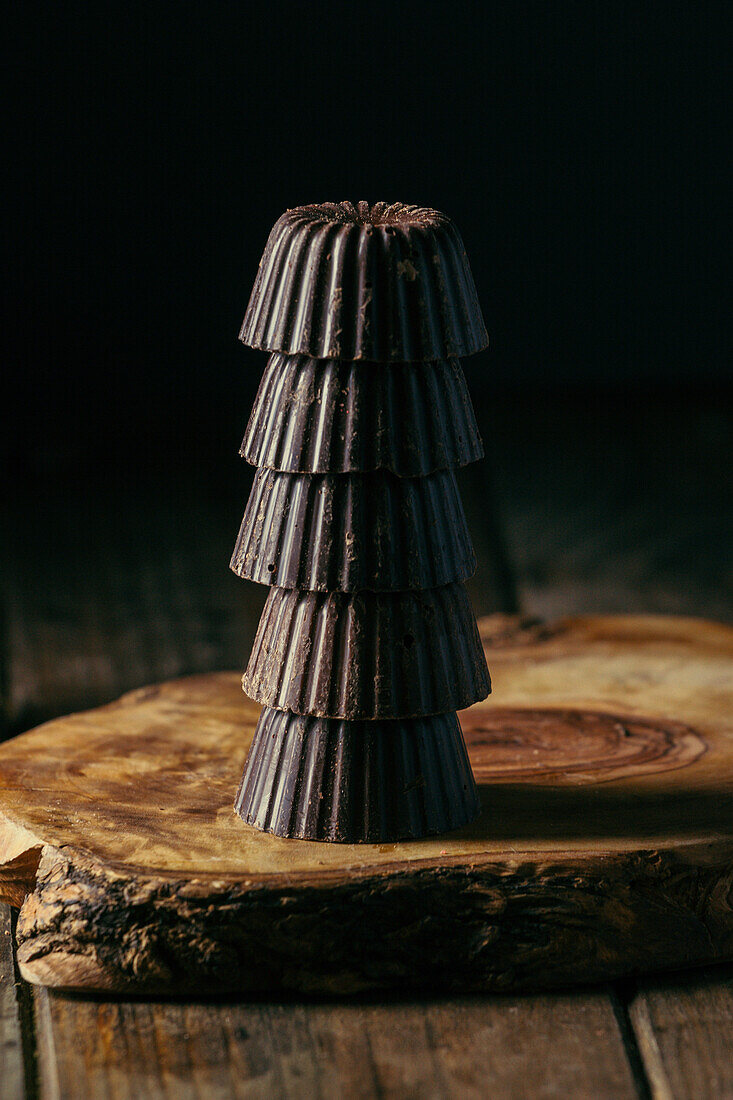 Appetizing dark chocolate pralines stacked on each other and served on wooden board against black background