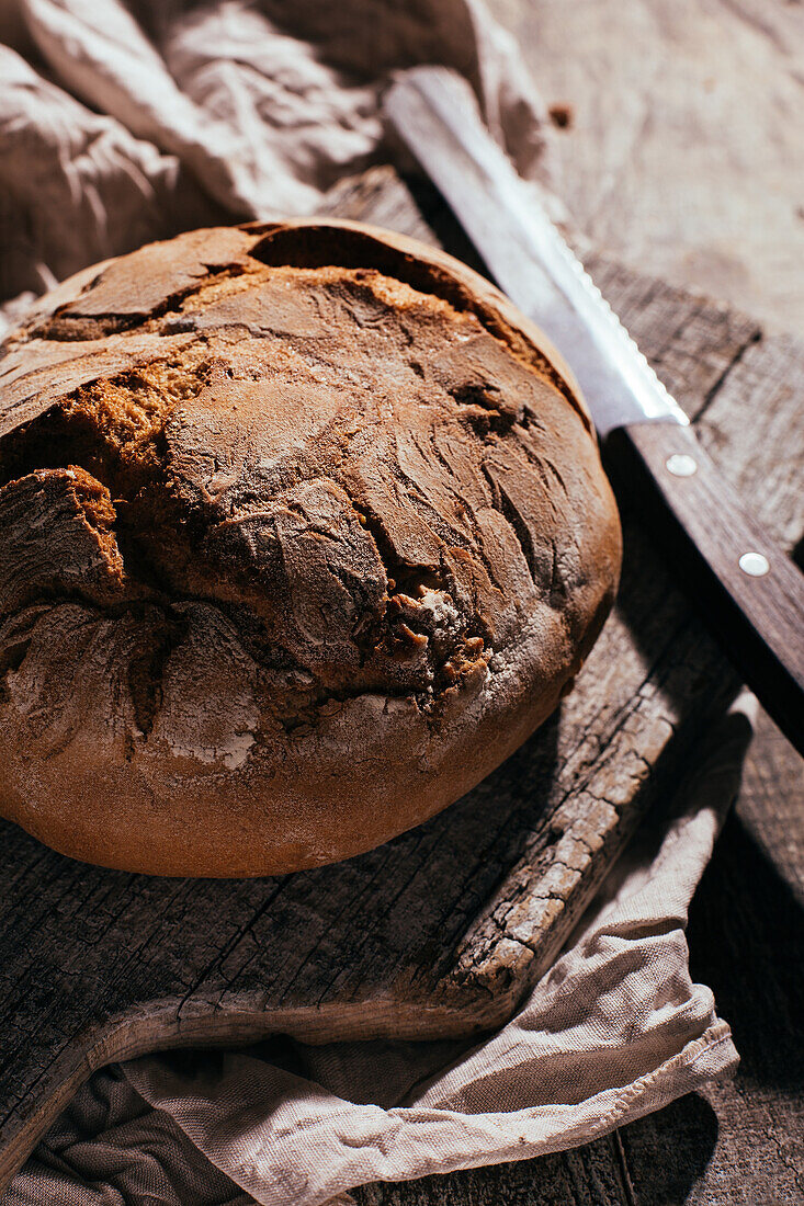 Köstliches frisch gebackenes Brot auf altem Schneidebrett auf einem Holztisch in der Küche von oben