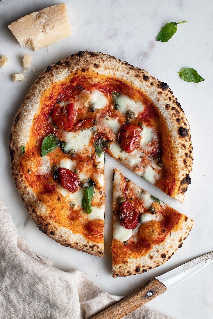 Draufsicht auf eine leckere Pizza mit Basilikum und Tomatensauce auf einem Holztisch neben einer Serviette in der Küche