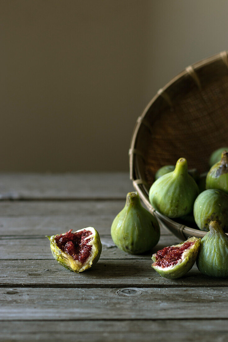 Closeup shot of basket with green figs and split fruit with red flesh on table