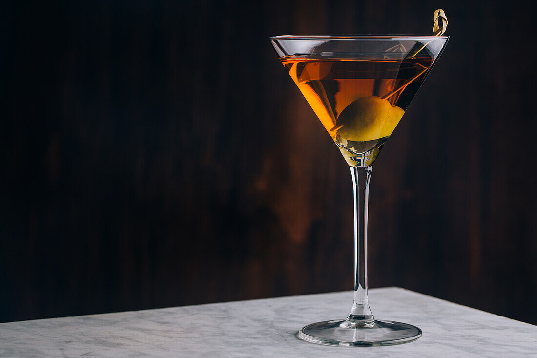 Glas mit Dirty-Martini-Cocktail, garniert mit grünen Oliven, auf einem Tisch serviert