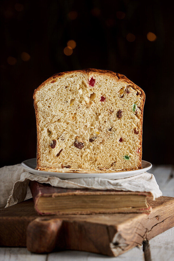 Still life of sliced fresh baked artisan Christmas panettone cake on vintage book and cutting board against dark background