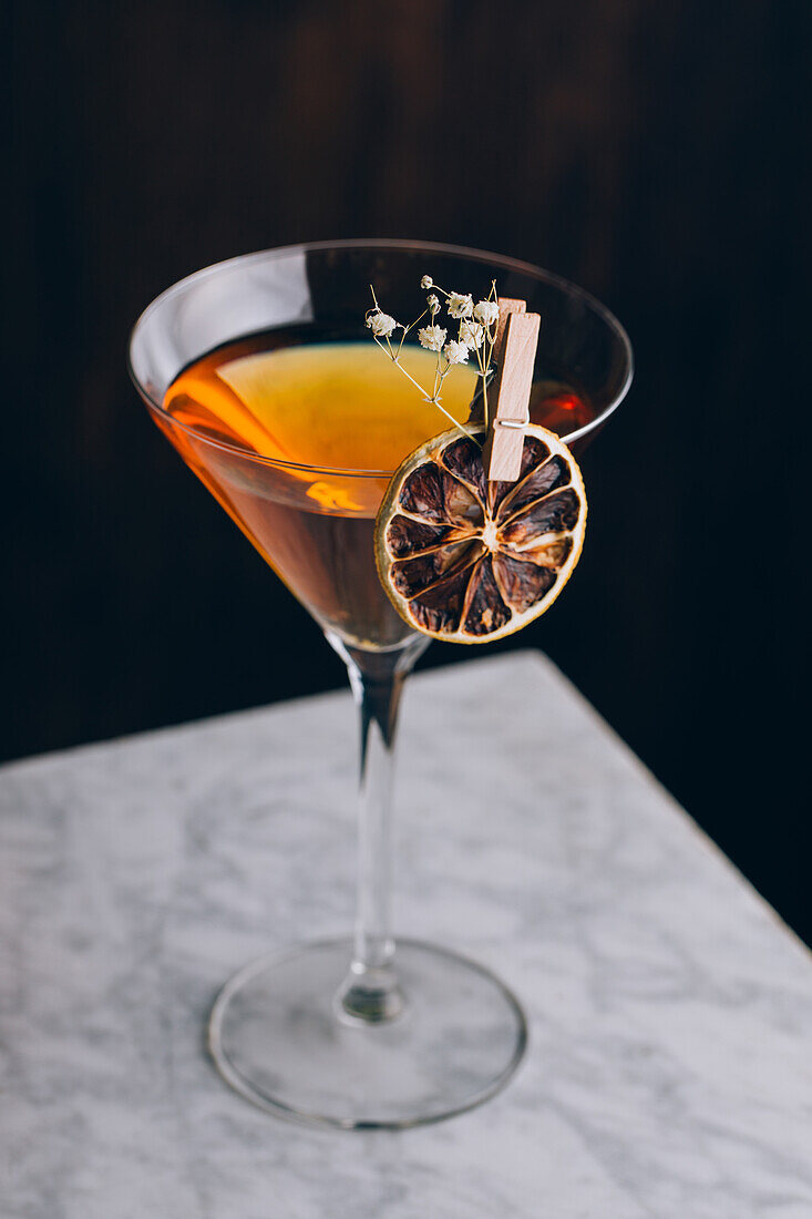 Glas eines traditionellen alkoholischen Manhattan-Cocktails, garniert mit einer Orangenscheibe und Blumen auf dem Tisch