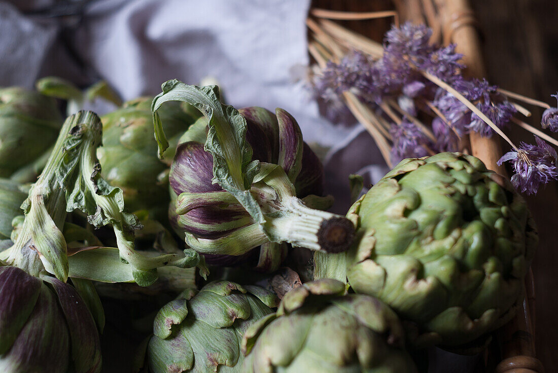 Closeup from above view of green artichokes laid in wicker basket with bunch of little purple flowers