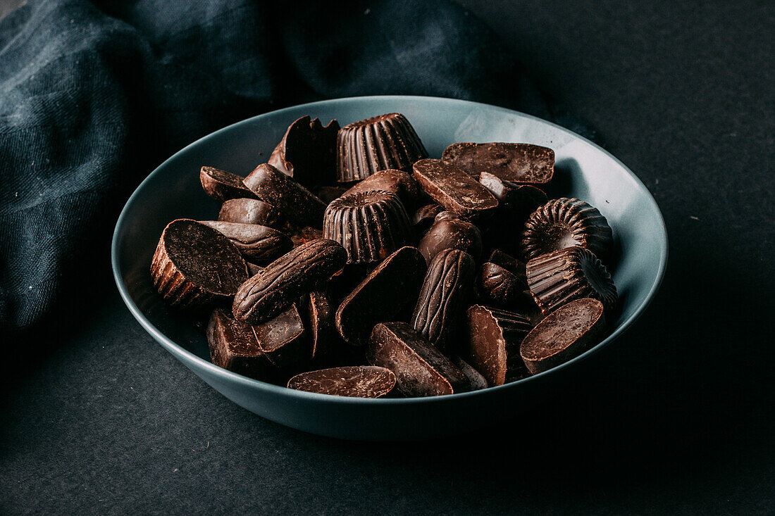 Verschiedene dunkle Schokoladentrüffel und Pralinen in verschiedenen Formen in einer Schale auf einem schwarzen Tisch
