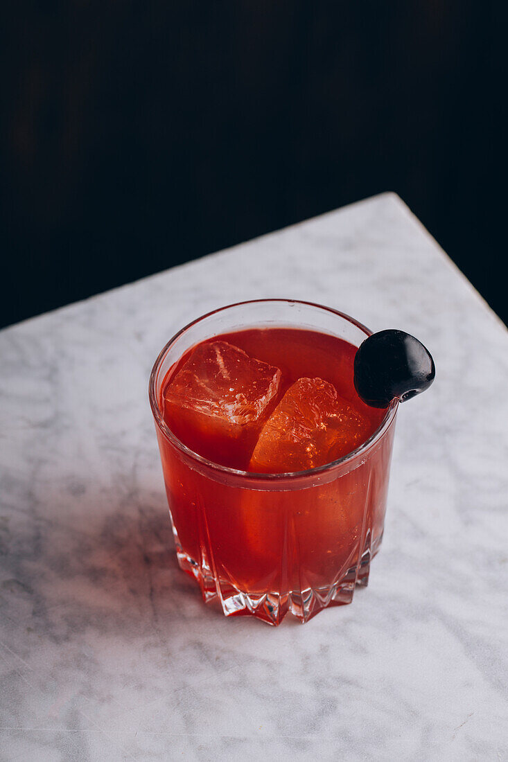 From above of glass of alcohol red Bloody Mary cocktail with ice cubes garnished with black olive served on table