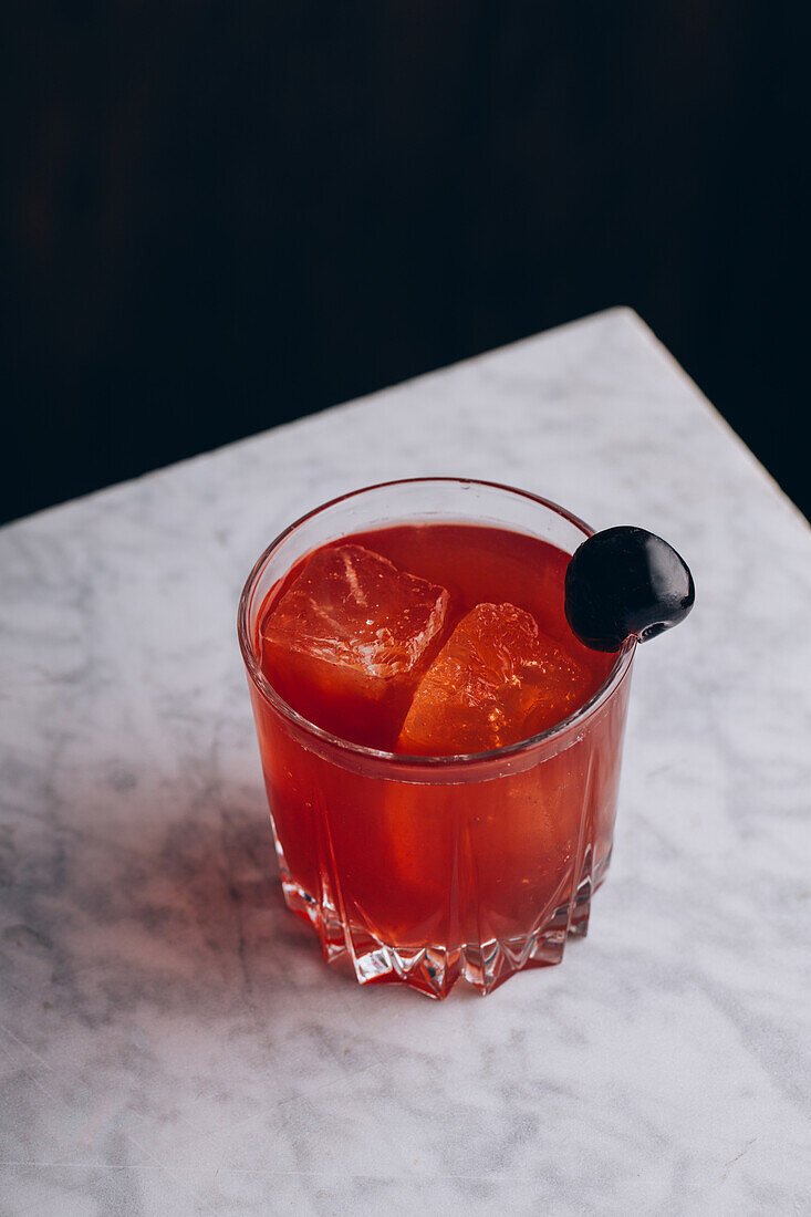Von oben ein Glas alkoholischer roter Bloody-Mary-Cocktail mit Eiswürfeln, garniert mit einer schwarzen Olive, serviert auf einem Tisch