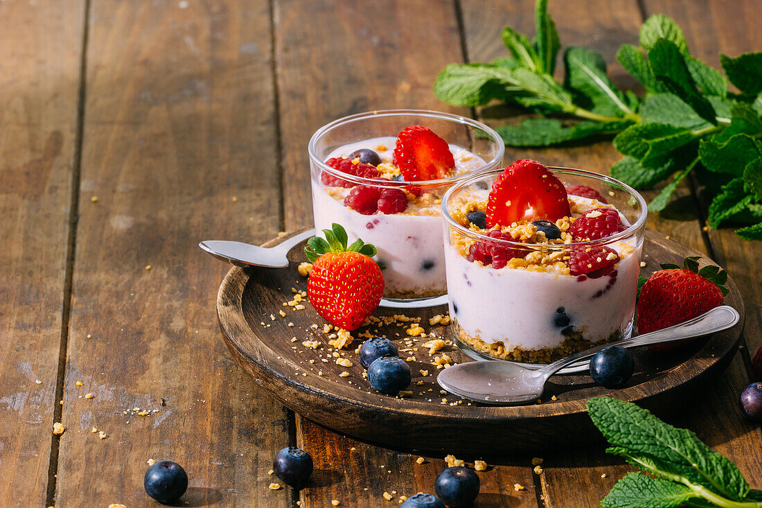 Von oben köstlicher hausgemachter Joghurt mit Erdbeeren, Beeren und Müsli auf Holztisch Hintergrund