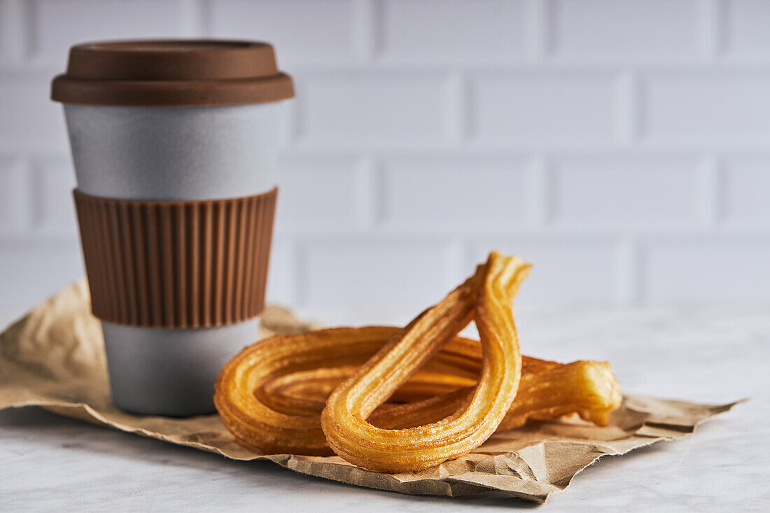 Fresh crispy churros and cup of hot coffee placed on table for breakfast