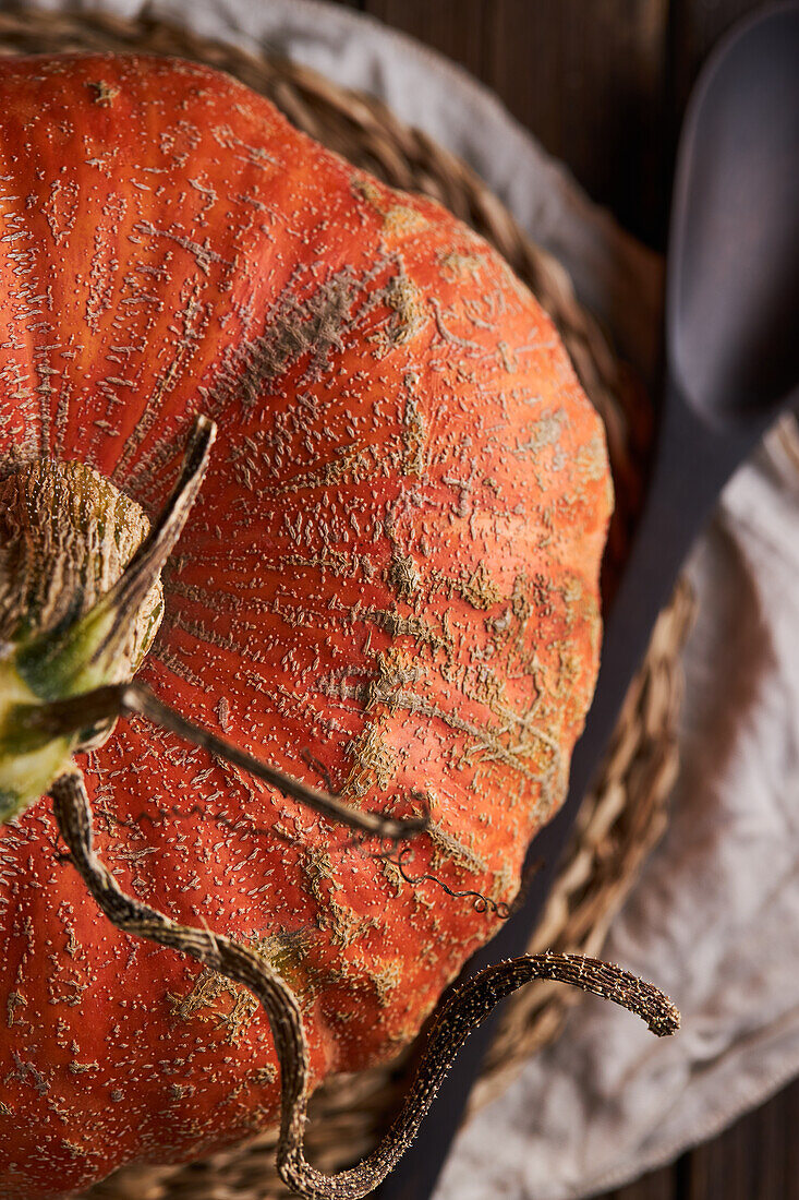 From above whole ripe pumpkin with slightly ribbed skin placed on wooden table on placemat against black background