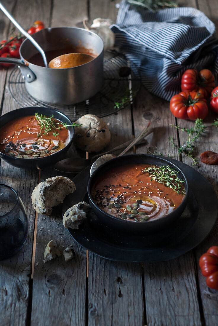 Composition of served bowls with delicious tomato creamy soup with seeds on table with tomatoes and bread buns