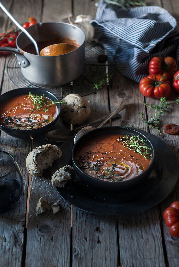 Komposition aus servierten Schalen mit köstlicher Tomatencremesuppe mit Kernen auf einem Tisch mit Tomaten und Brotbrötchen