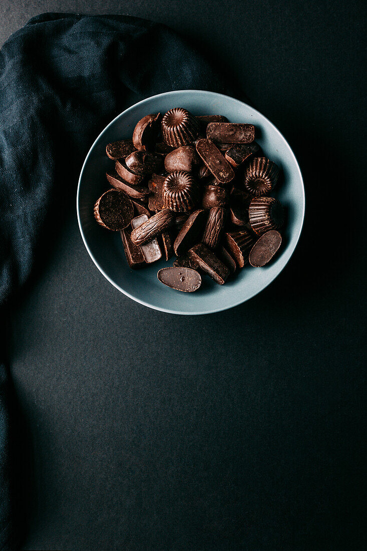 Top view of assorted dark chocolate truffles and pralines in various shapes in bowl placed on black table