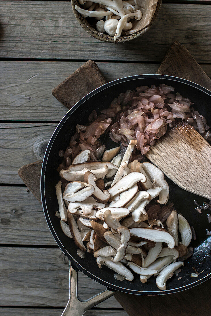 Top view of frying pot with sliced shiitake mushrooms and wood spatula on board