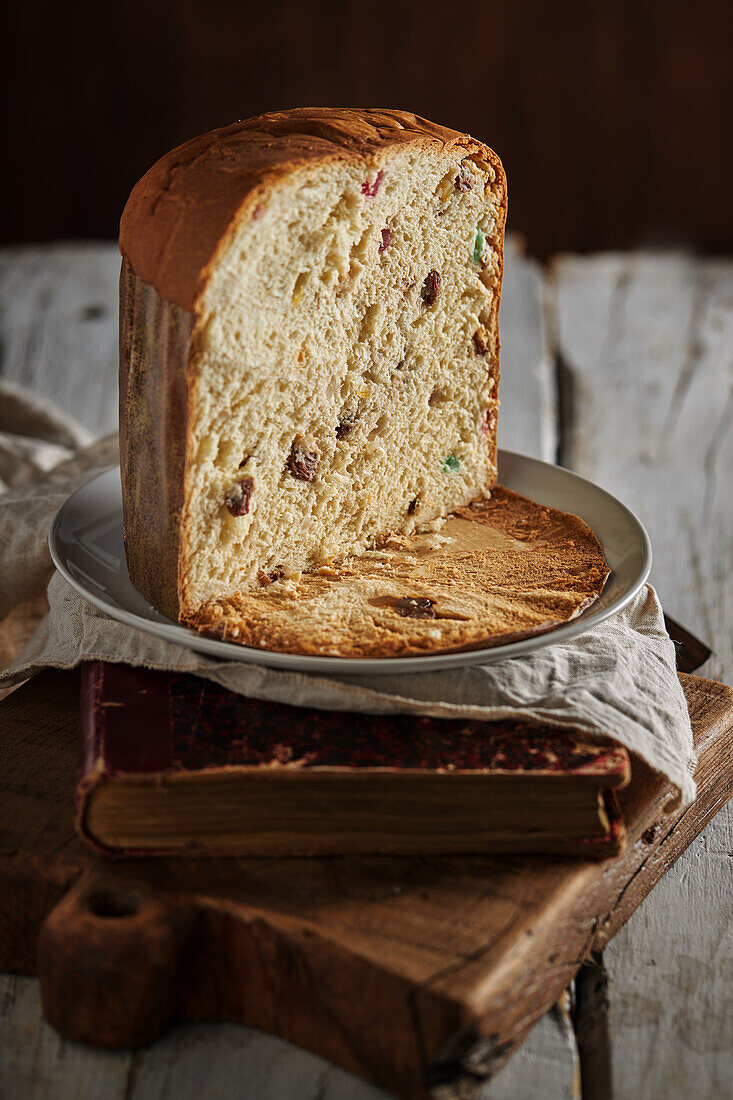 High angle still life of sliced fresh baked artisan Christmas panettone cake on vintage book and cutting board against dark background
