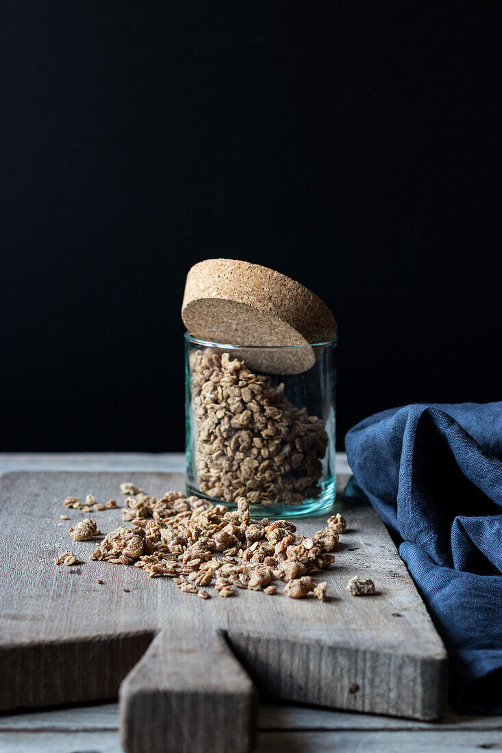 Glass jar with walnut granola laid on wooden chopping board on black background